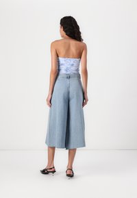 Svetlo modra breznaramna majica in široke denim culotte hlače. Hlače imajo surov rob in visok pas. Model nosi črne pete natikače.