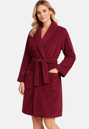 Frau trägt einen knielangen, burgunderfarbenen Fleece-Bademantel mit Schalkragen, zwei Vordertaschen und einem gebundenen Taillengürtel.