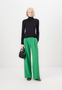 Pull à col montant noir à manches longues, pantalon large vert, sac à main noir texturé et chaussures à motifs. Tissu lisse et silhouette contemporaine.