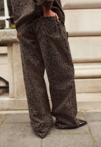 Pantalons larges à imprimé léopard en marron foncé avec des taches noires, dotés d'une poche arrière et d'une coupe décontractée, associés à des chaussures noires pointues.