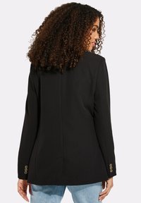 Černý blazer se strukturovaným designem, s přiléhavým střihem, dlouhými rukávy a zlatými knoflíky na manžetách. Hladká textilie.