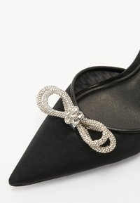 Chaussure noire en satin à bout pointu avec un nœud orné de strass. Matériau texturé avec une finition lisse. Design élégant et décoratif.