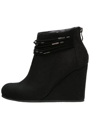 Bottes de cheville noires à talon compensé en daim doux, dotées d'un bout rond et de sangles décoratives noires avec des accents argentés autour de la cheville.