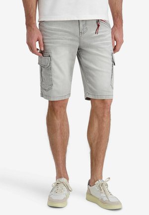 Man wearing light gray cargo shorts with side pockets and white sneakers, standing against a plain white background.