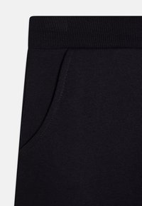 Dunkelblaue Sweatpants mit einem gerippten Bund, ausgestattet mit einer Seitentasche und einem glatten, strukturierten Stoff. Das Design betont Komfort und Funktionalität.
