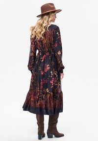 Długa, kwiecista sukienka z ciemnej tkaniny z falbaną u dołu, zdobiona czerwonymi i złotymi wzorami kwiatowymi, do tego brązowy kapelusz i brązowe kozaki za kolano.