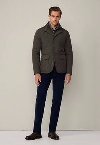 Gewatteerd olijfgroen jasje met een hoge kraag, twee zakken aan de voorkant en een knoopsluiting, gecombineerd met donkerblauwe broek en enkellaarsjes.