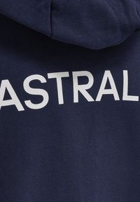 Marinblå hoodie med vit text "ASTRAL" på baksidan. Tyget verkar mjukt med en texturerad yta. Har en huva för extra värme.