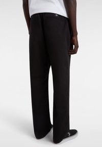 Black wide-leg pants made of lightweight fabric, featuring pockets and a subtle design. Paired with black slip-on shoes.