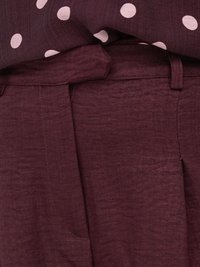 Gros plan sur un pantalon bordeaux avec braguette zippée et une chemise bordeaux à pois blancs rentrée à la taille.