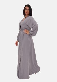 Robe maxi grise à manches longues avec un décolleté en V profond, fermeture à boutons, taille cintrée et tissu fluide. Texture douce et coupe décontractée.