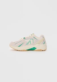 Sport sneaker in beige with green accents, mesh and synthetic upper, textured surface, rubber sole, and a chunky design.