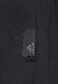 Svarta atletiska shorts med en tygetikett med en grå Adidas-logotyp, jämn struktur och enkel design. Inga synliga mönster eller detaljer.