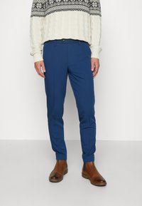 Blue tailored trousers with a smooth texture, featuring a slim fit and a single button closure, complemented by brown ankle boots.