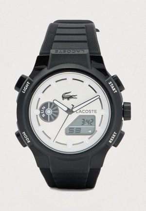 Montre Lacoste noire avec cadran blanc, affichages analogique et numérique, indicateur de jour et quatre boutons latéraux étiquetés Lumière, Mode, Démarrer et Réinitialiser.