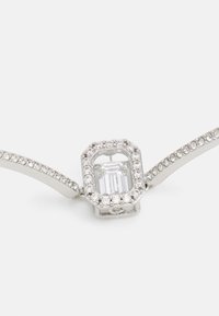 Srebrna zapestnica z osmerokotnim središčem, ki ga obkroža jasen pravokoten kamen, obdan z majhnimi okroglimi kristali. Gladek kovinski trak.