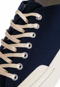 Sneaker blu in tela con lacci beige, occhielli metallici e suola in gomma bianca texturizzata. Focus sui dettagli della tomaia e della lacing.