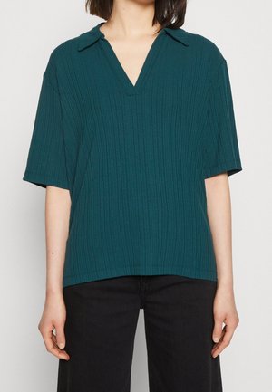 Haut côtelé à manches courtes de couleur bleu sarcelle avec col en V et col, doté d'une coupe décontractée et d'un ourlet droit, associé à un pantalon noir.