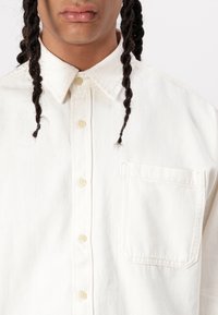 Camicia button-up color crema in denim con colletto, caratterizzata da dettagli di cucitura e una tasca sul petto.