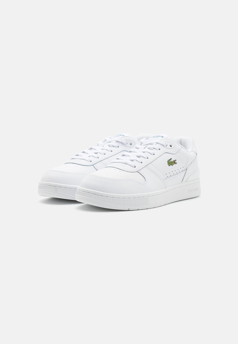 White sneakers featuring a smooth leather upper, perforated accents, flat laces, and a rubber outsole, with a small green logo on the side.