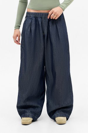 Pantalons larges en denim foncé avec une taille élastique, présentant des plis et une coupe décontractée. Fins aux extrémités et texture légère distincte.