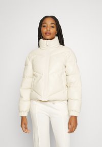 Cropped puffer jacket in cream color, featuring a high collar, front zipper, elastic cuffs, and geometric stitching patterns.