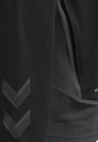 Pantalon de sport noir en tissu texturé, avec un côté lisse et un panneau à motif. Comprend un logo accentué et des détails en zigzag gris.