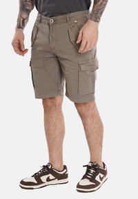 Bermuda cargo khaki in cotone, con diversi taschini, una vestibilità comoda e dettagli di cucitura a vista. Indossati con sneakers marroni e bianche.