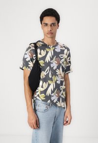 Tricou gri cu model floral, cu mâneci scurte, asortat cu blugi albaștri deschis și o geantă de umăr neagră. Material texturat cu culori vibrante.