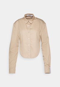 Chemise beige à manches longues avec boutons, col pointu et ourlet arrondi, présentée sur un fond uni clair.