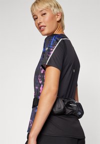 Camisa de desporto preta com um padrão abstrato colorido em roxo e azul, com mangas curtas e uma bolsa de cintura preta à volta da cintura.