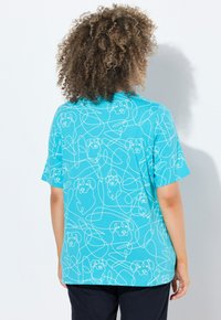 Camiseta de manga corta color turquesa con un dibujo lineal continuo en blanco de caras de perros, corte relajado, tejido suave, diseño casual.