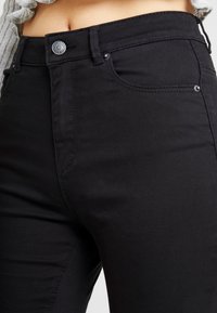 Jeans de tiro alto en un tejido elástico, con cierre de botón, dos bolsillos frontales y un sutil detalle de costura.