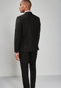 Sort jakkesæt med en figursyet jakke, hakket revers og enkelt slids bagpå. Slim-fit bukser fuldender det moderne design. Rene linjer og tekstureret stof.