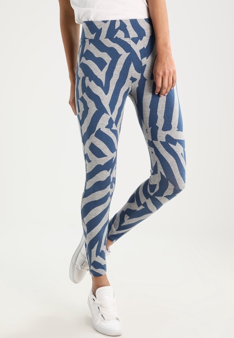 Leggings a righe zebra blu e grigie, realizzati in tessuto morbido con una vita alta, abbinati a sneaker bianche su uno sfondo neutro.