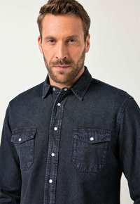 Camicia in denim scuro con chiusura a bottoni, due tasche sul petto, bottoni bianchi e un tessuto leggermente strutturato. Design con colletto e maniche lunghe.