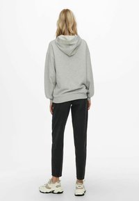 Felpa grigia con cappuccio, vestibilità oversize, polsini e orlo a coste, abbinata a pantaloni neri a sigaretta e sneakers beige. Design semplice con accenti minimi.