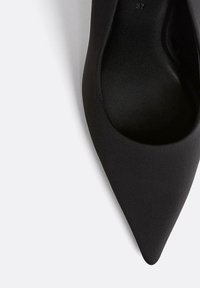 Scarpa con tacco alto a punta nera realizzata in materiale tessile liscio, caratterizzata da un design elegante con un interno testurizzato e una silhouette curva.