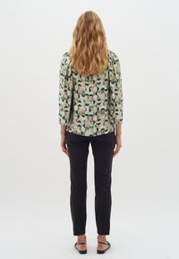 Bluză cu un model geometric în verde și bej, având mâneci bufante. Asortată cu pantaloni negri ajustați și sandale plate.