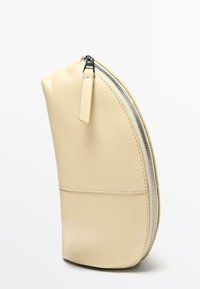 Beżowa skórzana saszetka o zaokrąglonym kształcie, z srebrnym zamkiem błyskawicznym i małą zawieszką. Gładka tekstura, bez widocznych wzorów czy dodatków.