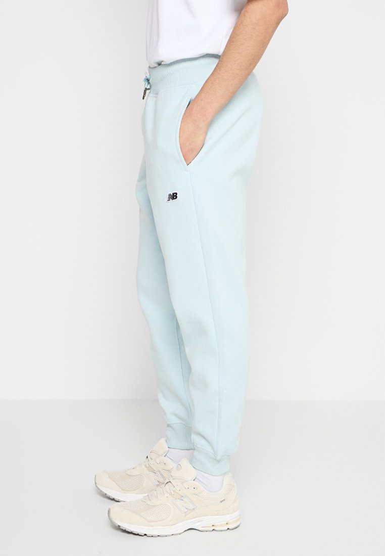 Pantalons de survêtement bleu clair avec taille élastique, poches latérales et un petit logo noir sur la cuisse gauche. Tissu doux avec une coupe décontractée.