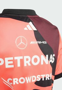 Jersey de manga corta en rosa y negro, hecho de tejido suave. Presenta logotipos de: Petronas, AMG y Adidas. Cuello negro con un diseño en contraste.