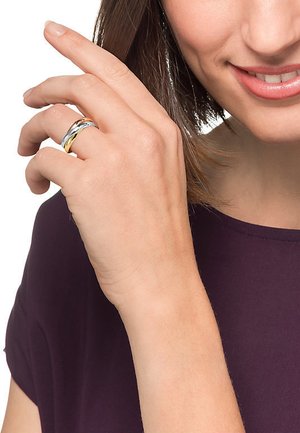 Drei miteinander verbundene Ringe aus Silber, Gold und Roségold mit einer glatten Oberfläche. Auf dem Ringfinger getragen, teilweise sichtbar Hand.
