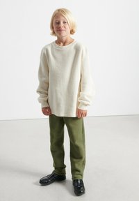 Off-white fleece långärmad tröja med rund hals, kombinerad med olivgröna mjuka byxor och svarta slip-on skor. Slät textur genomgående.