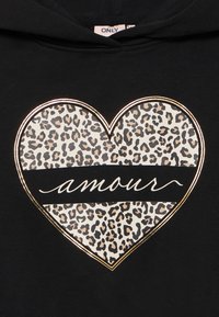 Svart hoodie med en stor hjärtgrafik i leopardtryck och en centrerad svart rand som säger "amour" i vit kursiv.