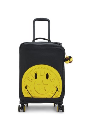 Valise noire à roulettes avec un grand motif texturé de smiley jaune, comportant une étoile au centre et un petit porte-clés jaune en fourrure.