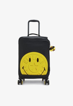 Black rolling suitcase with a large textured yellow smiley face design, featuring a star in the center and a small yellow furry keychain.