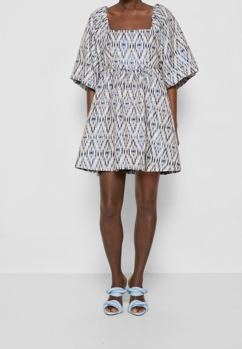 Kortärmad klänning med fyrkantig halsringning i mönstrad tyg i blått och vitt. Utställd kjol, med matchande ljusblå flätade sandaler.
