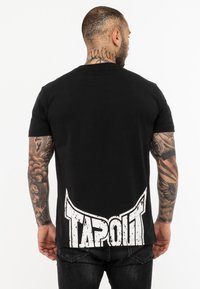 Fekete pamut póló, hátulján nagy fehér "TAPOUT" logóval, rövid ujjakkal és standard illeszkedésű fazonnal.