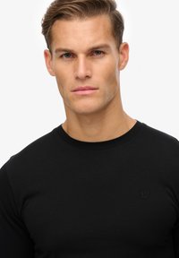 Zwarte langemouwen t-shirt van katoen, met een ronde halslijn en een klein logo geborduurd op de borst. Glad textuur.